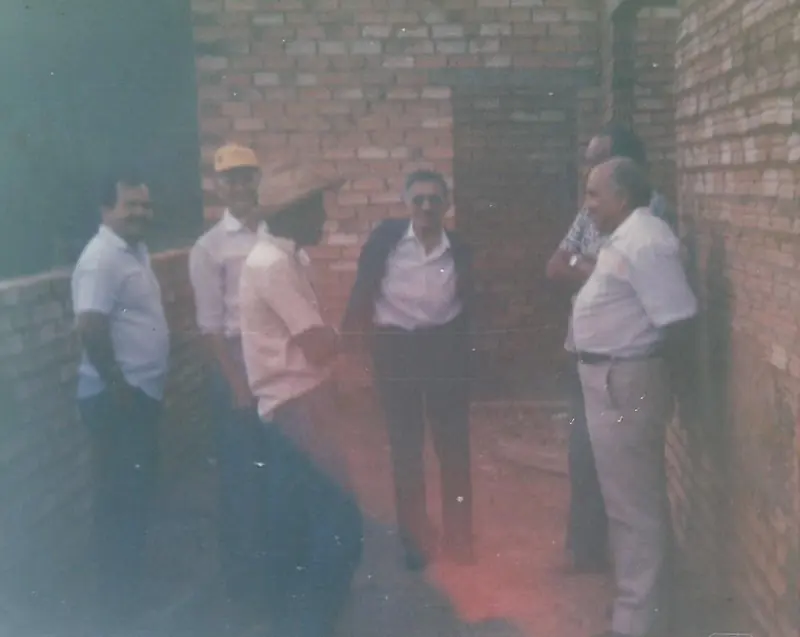 Seis homens conversando entre paredes de tijolos de uma construção ainda sem reboco, com carimbo MAI/91 no canto.